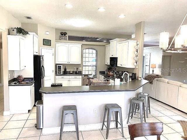 11315 Cypress Shore Ct, Clermont, FL 34711 - kitchen featuring dark countertops, a peninsula, white cabinets, a kitchen breakfast bar, and black appliances