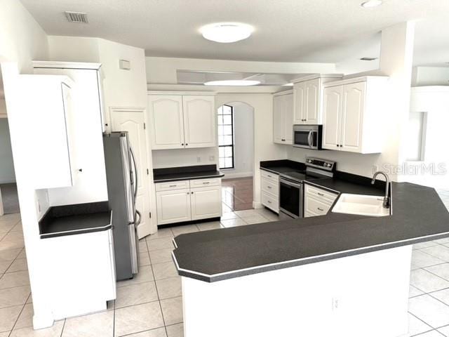 11315 Cypress Shore Ct, Clermont, FL 34711 - kitchen featuring appliances with stainless steel finishes, a sink, a peninsula, light tile patterned floors, and arched walkways