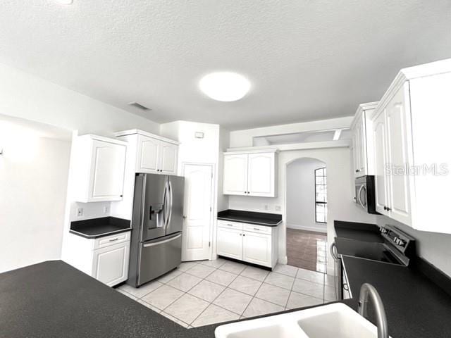 11315 Cypress Shore Ct, Clermont, FL 34711 - kitchen with appliances with stainless steel finishes, dark countertops, arched walkways, white cabinets, and light tile patterned floors
