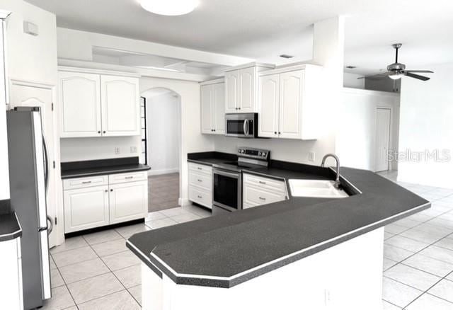 11315 Cypress Shore Ct, Clermont, FL 34711 - kitchen featuring stainless steel appliances, a sink, arched walkways, dark countertops, and a peninsula