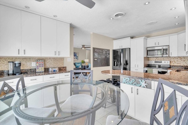 6731 Washington Pl, Bradenton, FL 34207 - kitchen featuring appliances with stainless steel finishes, a ceiling fan, dark stone counters, a textured ceiling, and a peninsula