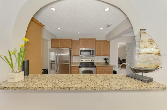 74 Windsor Dr, Englewood, FL 34223 - kitchen featuring appliances with stainless steel finishes, recessed lighting, a peninsula, light stone countertops, and arched walkways
