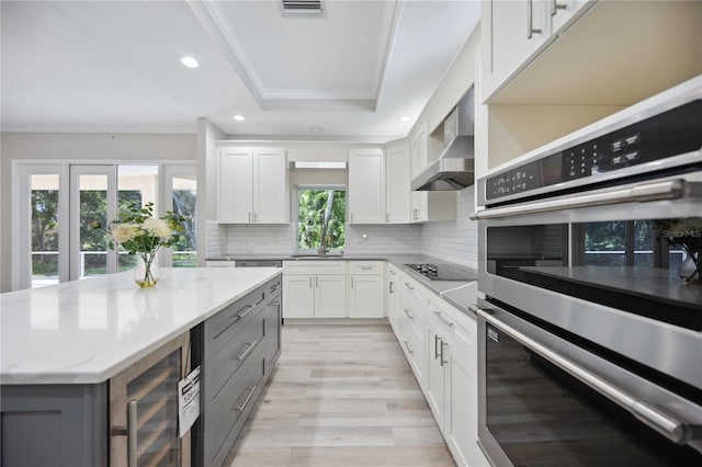 5018 Hanging Moss Ln, Sarasota, FL 34238 - kitchen featuring gray cabinets, double oven, ornamental molding, tasteful backsplash, and wall chimney range hood