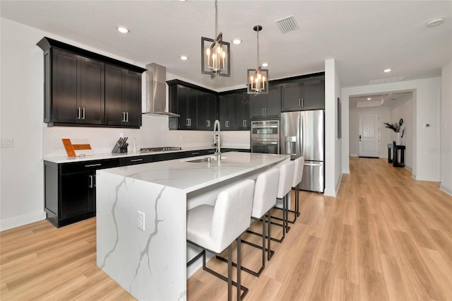 17333 Savory Mist Cir, Bradenton, FL 34211 - kitchen featuring stainless steel appliances, wall chimney range hood, a chandelier, light stone counters, and light wood-style floors