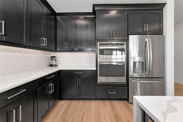 17333 Savory Mist Cir, Bradenton, FL 34211 - kitchen featuring appliances with stainless steel finishes, dark cabinets, light wood finished floors, backsplash, and light stone countertops