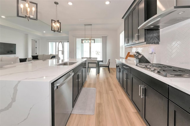 17333 Savory Mist Cir, Bradenton, FL 34211 - kitchen featuring appliances with stainless steel finishes, wall chimney range hood, a sink, decorative backsplash, and light wood-style flooring