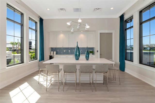 17333 Savory Mist Cir, Bradenton, FL 34211 - kitchen featuring healthy amount of natural light, white cabinetry, tasteful backsplash, light wood-style flooring, and crown molding