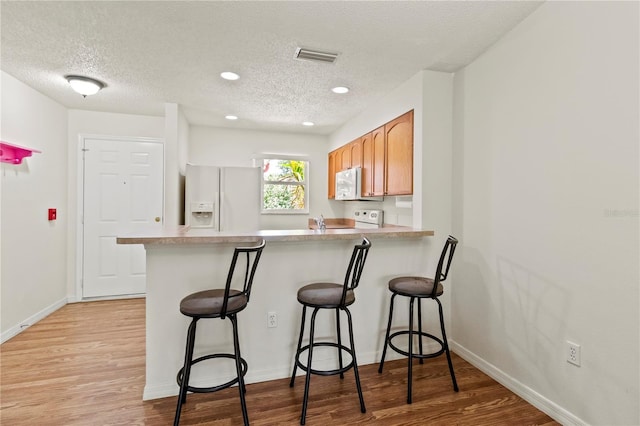 5500 Longwood Run Blvd Unit 203, Sarasota, FL 34243 - kitchen with white appliances, a textured ceiling, a peninsula, light wood-type flooring, and a breakfast bar area