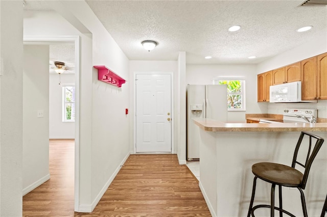 5500 Longwood Run Blvd Unit 203, Sarasota, FL 34243 - kitchen with white appliances, light wood-type flooring, a breakfast bar area, a textured ceiling, and ceiling fan