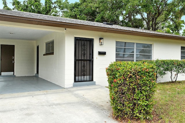 1354 22nd St, Sarasota, FL 34234 - doorway to property with an attached carport, concrete block siding, roof with shingles, and concrete driveway
