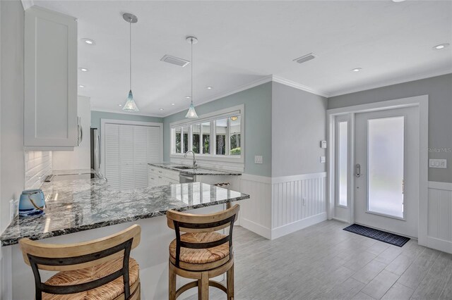 139 Vista Hermosa Cir, Sarasota, FL 34242 - kitchen featuring stone countertops, white cabinetry, light wood-style flooring, a wainscoted wall, and a peninsula