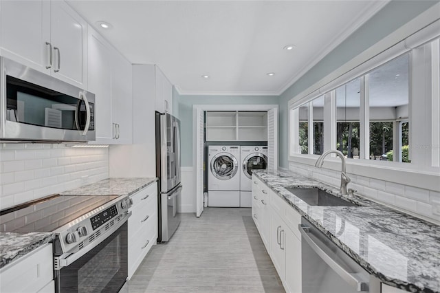 139 Vista Hermosa Cir, Sarasota, FL 34242 - kitchen featuring appliances with stainless steel finishes, washer and dryer, white cabinetry, decorative backsplash, and ornamental molding