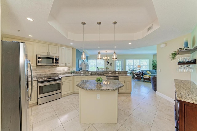 7820 34th Ave W Unit 102, Bradenton, FL 34209 - kitchen with appliances with stainless steel finishes, a peninsula, a tray ceiling, open floor plan, and light stone countertops