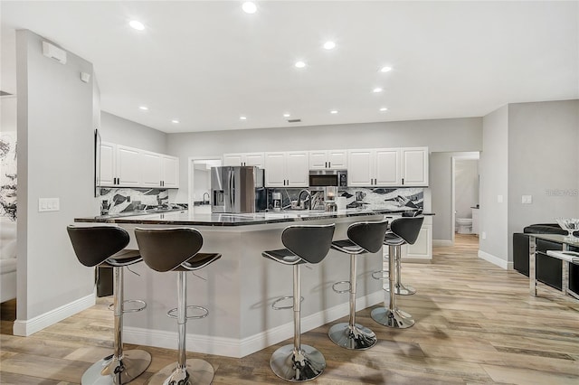 2912 51st St E, Bradenton, FL 34208 - kitchen with appliances with stainless steel finishes, a breakfast bar, backsplash, light wood-style flooring, and white cabinetry