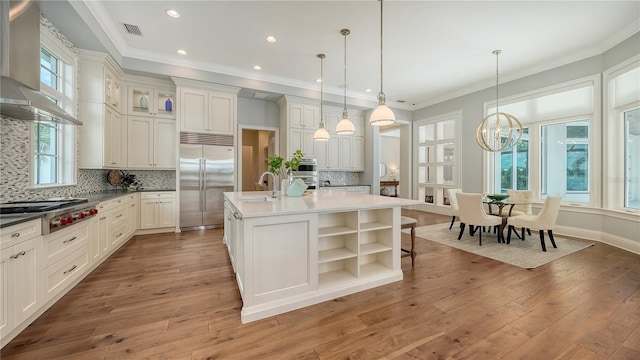 14665 Como Cir, Lakewood Ranch, FL 34202 - kitchen featuring stainless steel appliances, wall chimney range hood, open shelves, an island with sink, and light wood-style floors