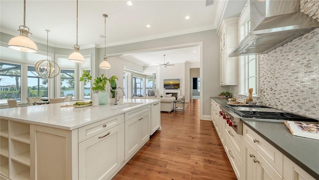 14665 Como Cir, Lakewood Ranch, FL 34202 - kitchen featuring wall chimney exhaust hood, stainless steel gas stovetop, wood finished floors, backsplash, and ornamental molding