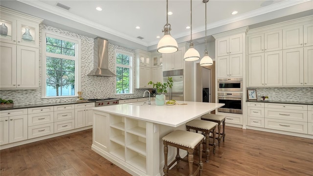 14665 Como Cir, Lakewood Ranch, FL 34202 - kitchen featuring appliances with stainless steel finishes, wall chimney range hood, dark wood-style flooring, tasteful backsplash, and ornamental molding