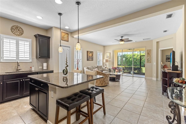 2070 Crystal Lake Trl, Bradenton, FL 34211 - kitchen featuring a kitchen bar, a kitchen island, tasteful backsplash, light tile patterned floors, and dark stone counters