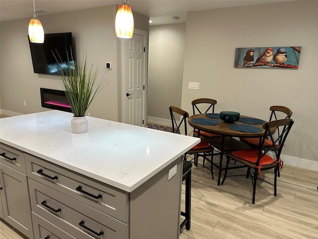 1840 3rd Ave E, Bradenton, FL 34208 - kitchen with gray cabinetry, light wood-type flooring, pendant lighting, a center island, and a glass covered fireplace