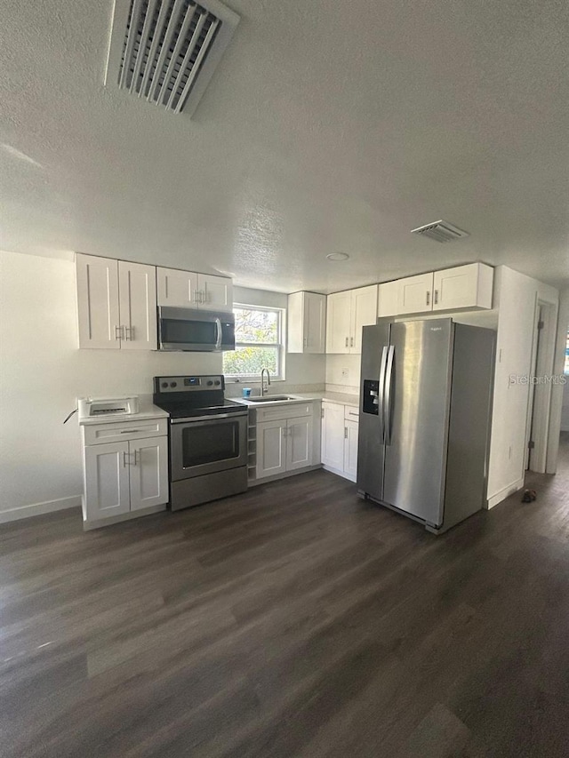 4740 Garcia Ave, Sarasota, FL 34233 - kitchen with appliances with stainless steel finishes, a textured ceiling, white cabinetry, dark wood-type flooring, and light countertops
