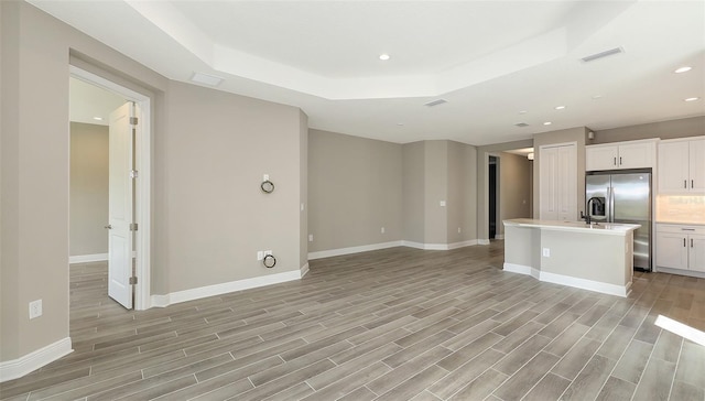 2321 Blue Mahoe Ln, Sarasota, FL 34240 - unfurnished living room featuring a raised ceiling, recessed lighting, light wood-style floors, and baseboards