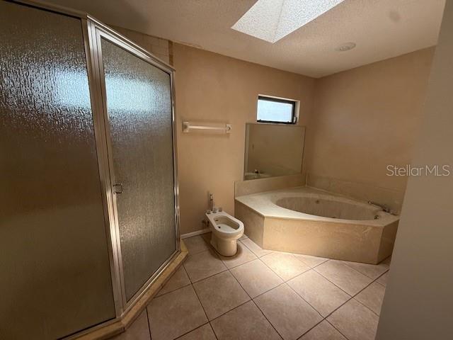5032 81st Avenue Terrace E, Sarasota, FL 34243 - full bathroom with a skylight, a stall shower, tile patterned flooring, a bidet, and a garden tub