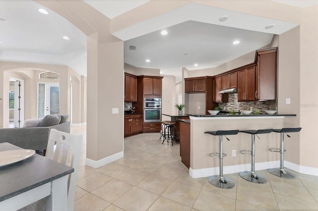 13503 22nd Ct E, Parrish, FL 34219 - kitchen with arched walkways, dark countertops, stainless steel double oven, a kitchen bar, and recessed lighting