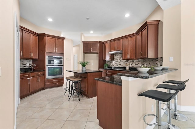 13503 22nd Ct E, Parrish, FL 34219 - kitchen featuring double oven, under cabinet range hood, decorative backsplash, a breakfast bar area, and a peninsula