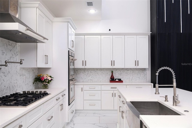 1841 Moorings Ct, Clermont, FL 34711 - kitchen featuring wall chimney range hood, gas stovetop, white cabinetry, light marble finish floors, and double oven
