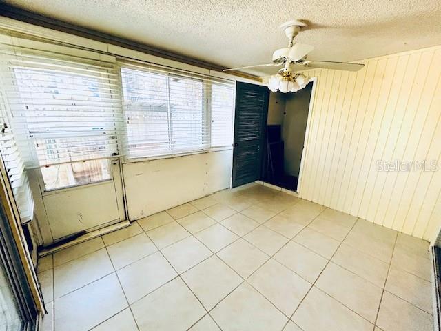 2607 29th Ave W, Bradenton, FL 34205 - spare room with a textured ceiling, healthy amount of natural light, ceiling fan, light tile patterned floors, and wood walls