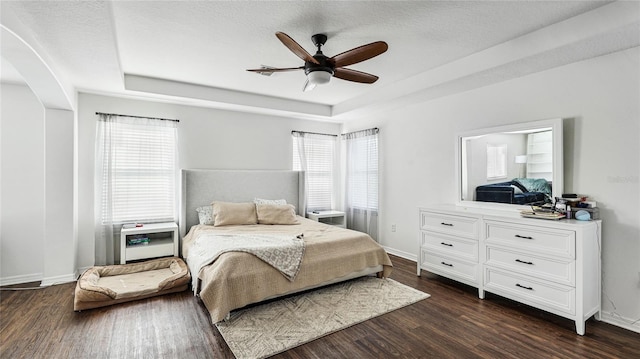 8804 Founders Cir, Palmetto, FL 34221 - bedroom featuring a tray ceiling, arched walkways, multiple windows, dark wood-style flooring, and a textured ceiling