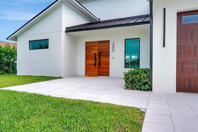 289 Long Meadow Ln, Rotonda West, FL 33947 - doorway to property featuring stucco siding, a standing seam roof, metal roof, and a lawn