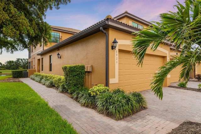 6923 Grand Estuary Trl Unit 101, Bradenton, FL 34212 - property exterior at dusk with stucco siding, a garage, decorative driveway, and a tile roof