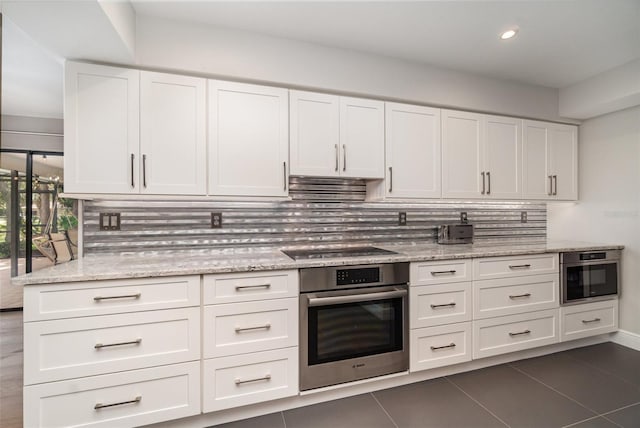4353 Indian Point Trl, Sarasota, FL 34238 - kitchen featuring stainless steel oven, white cabinetry, backsplash, light stone countertops, and dark tile patterned flooring