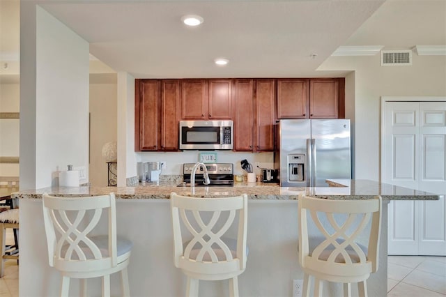 5528 Palmer Cir Unit 104, Bradenton, FL 34211 - kitchen featuring stainless steel appliances, brown cabinetry, light stone counters, light tile patterned floors, and crown molding