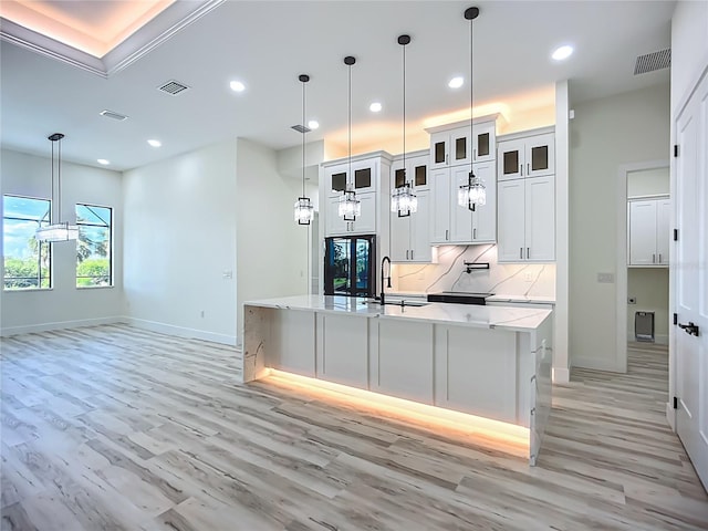 1167 Boundary Blvd, Rotonda West, FL 33947 - kitchen with light wood finished floors, recessed lighting, a kitchen island with sink, decorative backsplash, and white cabinetry