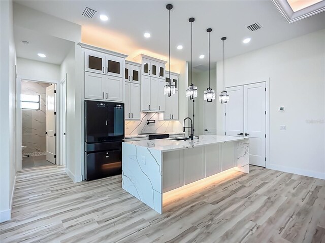 1167 Boundary Blvd, Rotonda West, FL 33947 - kitchen featuring freestanding refrigerator, light wood-style floors, a center island with sink, light stone countertops, and glass insert cabinets
