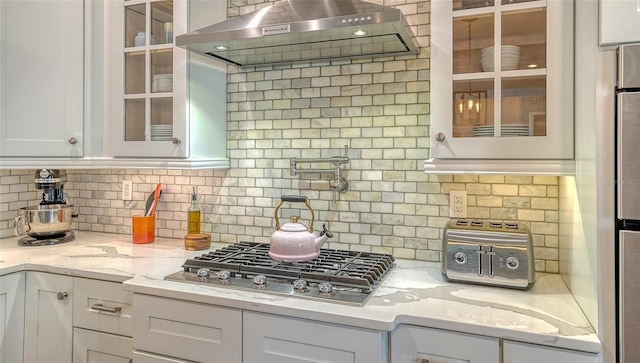 13220 Swiftwater Way, Lakewood Ranch, FL 34211 - kitchen with wall chimney exhaust hood, white cabinets, stainless steel gas stovetop, backsplash, and glass insert cabinets