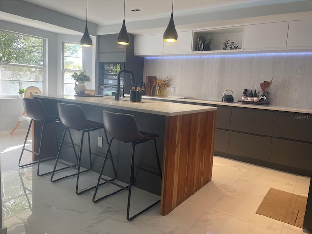 5848 Milton Ave, Sarasota, FL 34243 - kitchen with modern cabinets, light marble finish flooring, a breakfast bar area, light countertops, and an island with sink