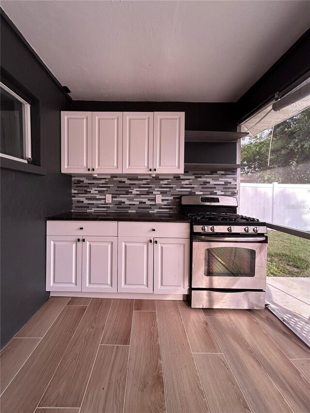 5848 Milton Ave, Sarasota, FL 34243 - kitchen with gas stove, white cabinetry, tasteful backsplash, dark countertops, and wood finished floors