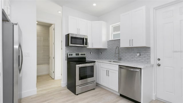 4796 Duncan Rd, Punta Gorda, FL 33982 - kitchen featuring stainless steel appliances, white cabinetry, backsplash, light wood-type flooring, and light stone countertops