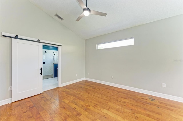 6423 Royal Tern Cir, Lakewood Ranch, FL 34202 - unfurnished bedroom with light wood-style floors, lofted ceiling, a barn door, a ceiling fan, and a textured ceiling