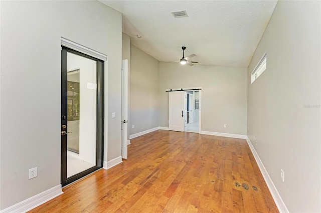 6423 Royal Tern Cir, Lakewood Ranch, FL 34202 - empty room with vaulted ceiling, ceiling fan, light wood-style flooring, a barn door, and a textured ceiling