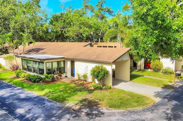 6832 Woodwind Dr Unit 53, Sarasota, FL 34231 - mid-century modern home with concrete driveway, a shingled roof, stucco siding, an attached carport, and a front lawn