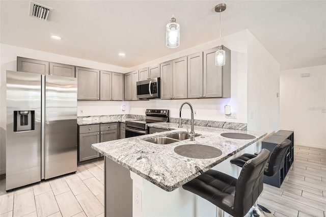 718 17th St E, Bradenton, FL 34208 - kitchen featuring appliances with stainless steel finishes, a peninsula, light stone counters, gray cabinetry, and decorative light fixtures