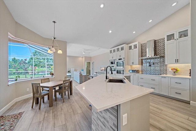5523 Secluded Oaks Way, Sarasota, FL 34233 - kitchen with wall chimney range hood, double oven, vaulted ceiling, an island with sink, and light wood-style floors
