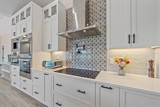 5523 Secluded Oaks Way, Sarasota, FL 34233 - kitchen featuring wall chimney range hood, black electric stovetop, backsplash, and stainless steel double oven