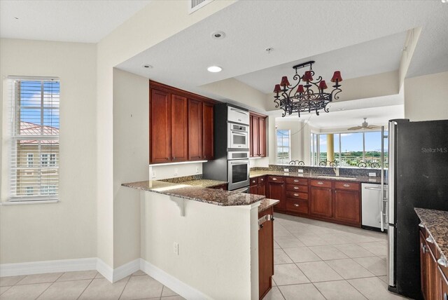 5100 Jessie Harbor Dr Unit 701, Osprey, FL 34229 - kitchen with stainless steel appliances, a peninsula, dark stone countertops, light tile patterned floors, and a kitchen bar