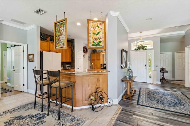 315 36th St NE, Bradenton, FL 34208 - kitchen with ornamental molding, a peninsula, freestanding refrigerator, a kitchen breakfast bar, and brown cabinets