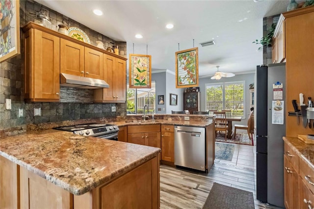 315 36th St NE, Bradenton, FL 34208 - kitchen with appliances with stainless steel finishes, a peninsula, under cabinet range hood, ornamental molding, and brown cabinets